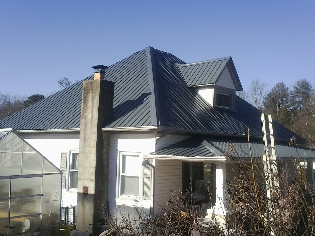 Dark blue standing seam metal roof on a white farmhouse with dormer — Slate & Tile Roof Repair by Roofing Brothers in Cedar Crest