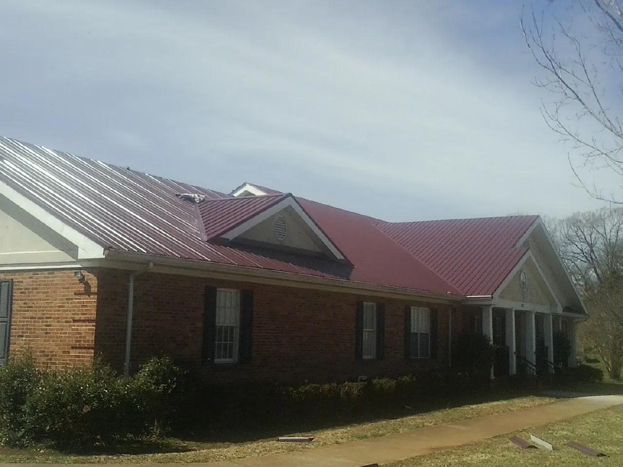 Red metal roof with gabled entries on a long brick building, from a Hail Damage Roof Repair job in Cedar Crest