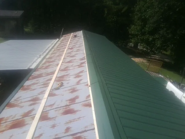 Old rusted panels beside newly installed green metal roofing — Wind Damage Roof Repair by Roofing Brothers in Cedar Crest