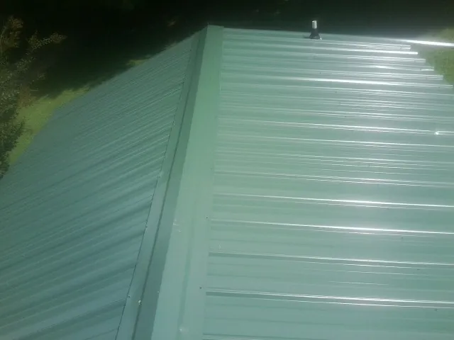 New green metal panels meeting at the ridge of a roof — Flat Roof Repair work by our crew in Cedar Crest