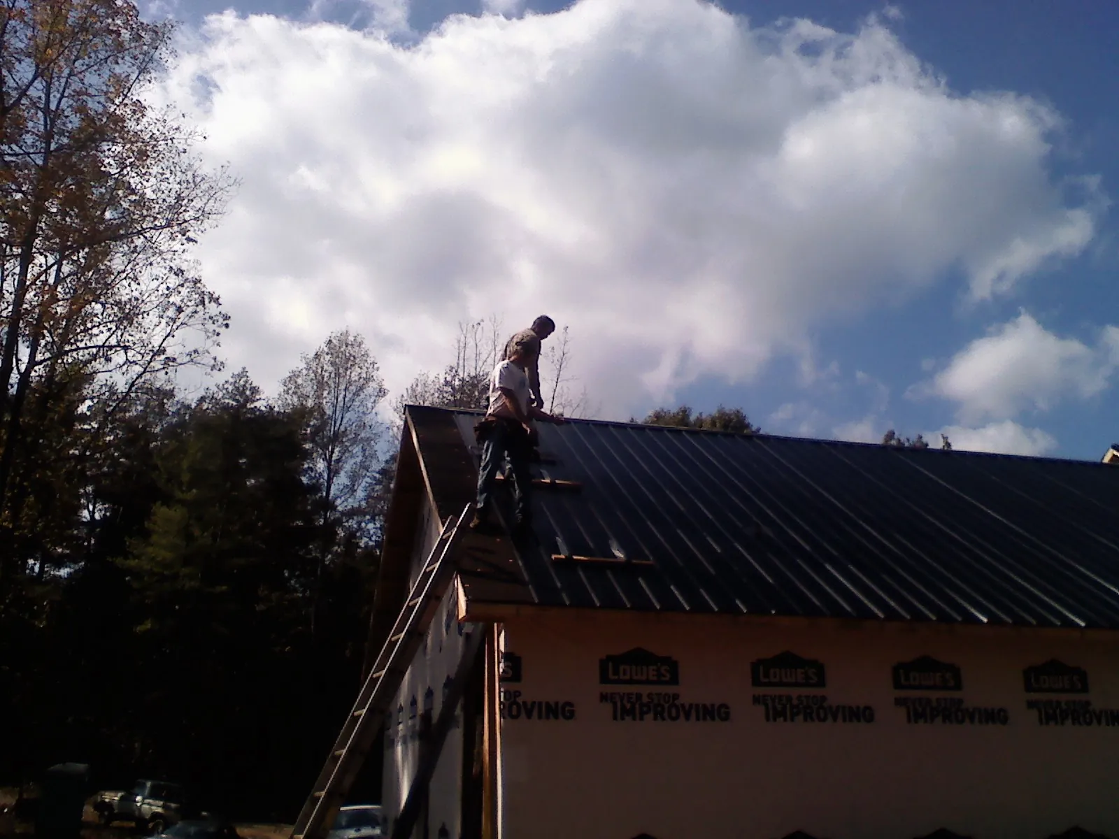 Roofer fastening dark metal panels high against a cloudy sky, from a Roof Inspection job in Cedar Crest
