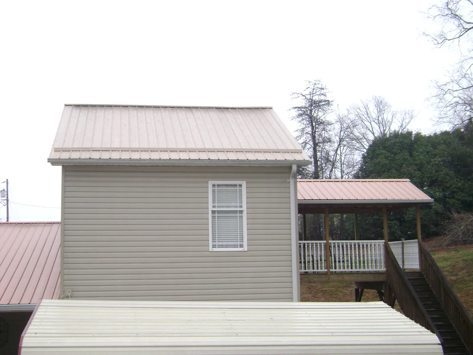 Tan metal roofs on a two story addition and attached porch, from a Roof Replacement job in Cedar Crest